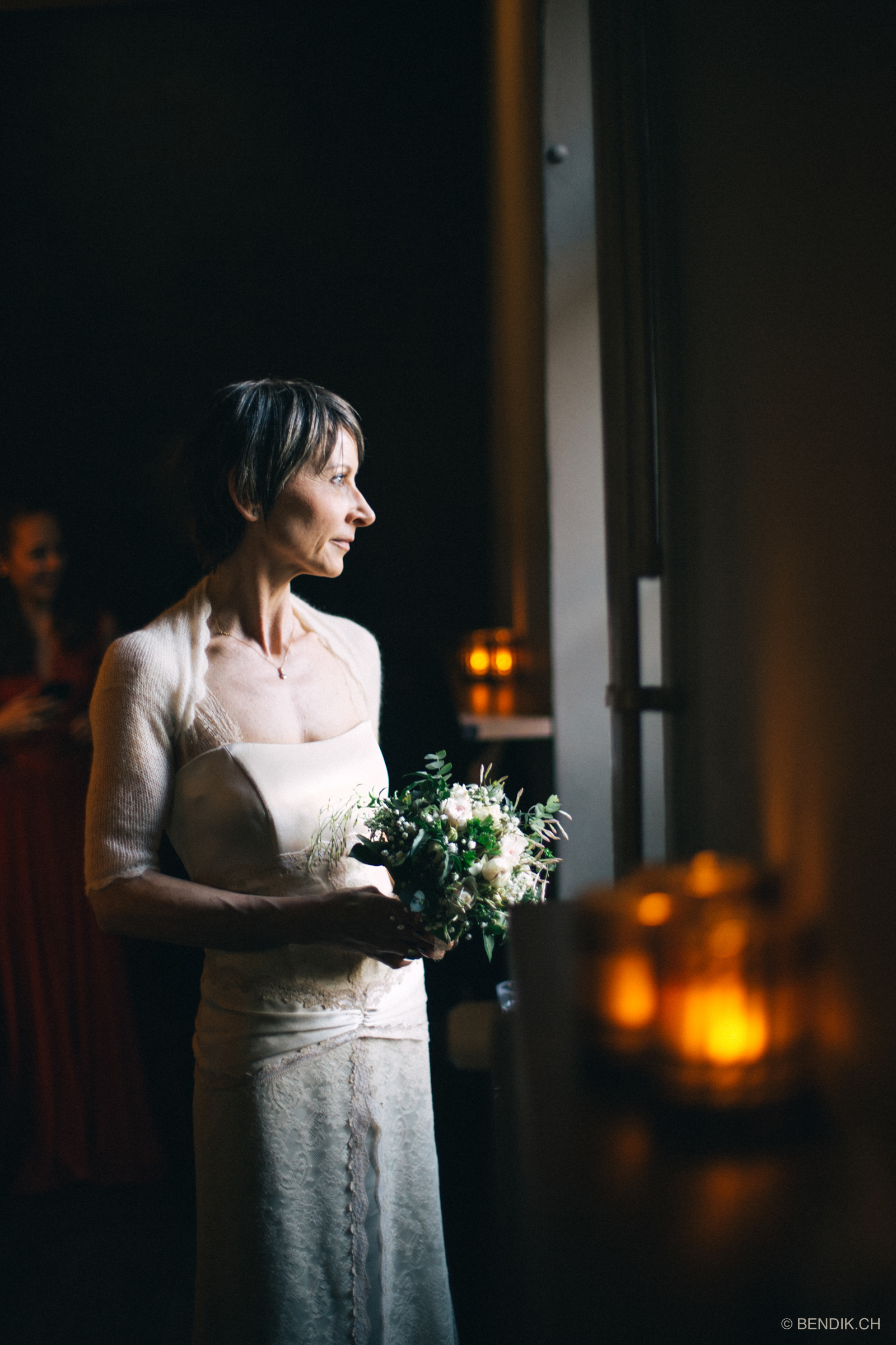 Braut sieht aus dem Fenster mit Brautstrauss in der Hand