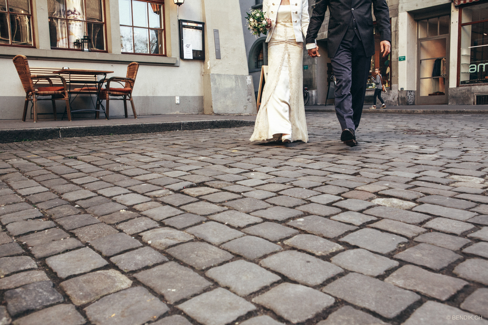 Brautpaar schreitet mit Brautstrauss Pflastersteinplatz entlang